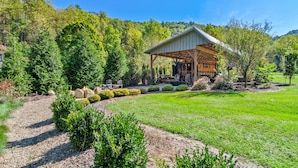 A rustic cabin with a covered porch, surrounded by a well-maintained garden and a forested hillside.