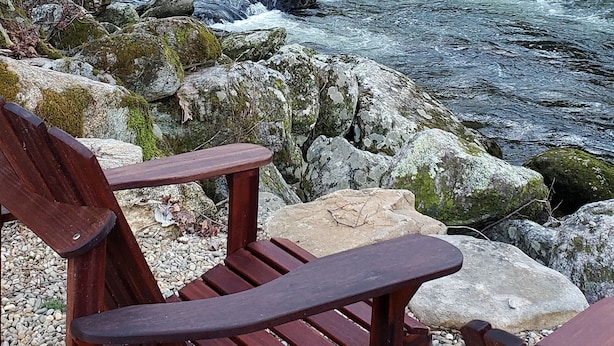 A wooden bench overlooking a flowing river with rocks and trees in the background.