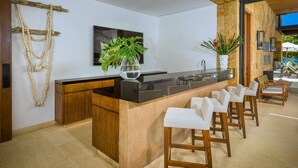 Een moderne keuken met een centraal eiland, houten barstoelen, een hangende plant en een lijstwerkkunstwerk aan de muur.