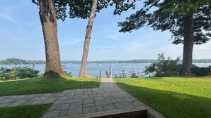 Un chemin pavé mène à une zone herbeuse bordée d’arbres, d’où l’on peut admirer un lac.