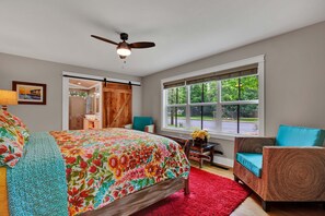 Une chambre à coucher avec un lit, une chaise, un bureau, une fenêtre et un ventilateur de plafond.