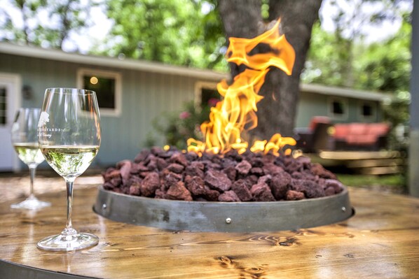 Una hoguera con leña ardiendo, dos copas de vino blanco y una mesa de madera.