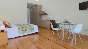 A modern room with a bed, a dining table with chairs, a TV mounted on the wall, and a kitchen area.