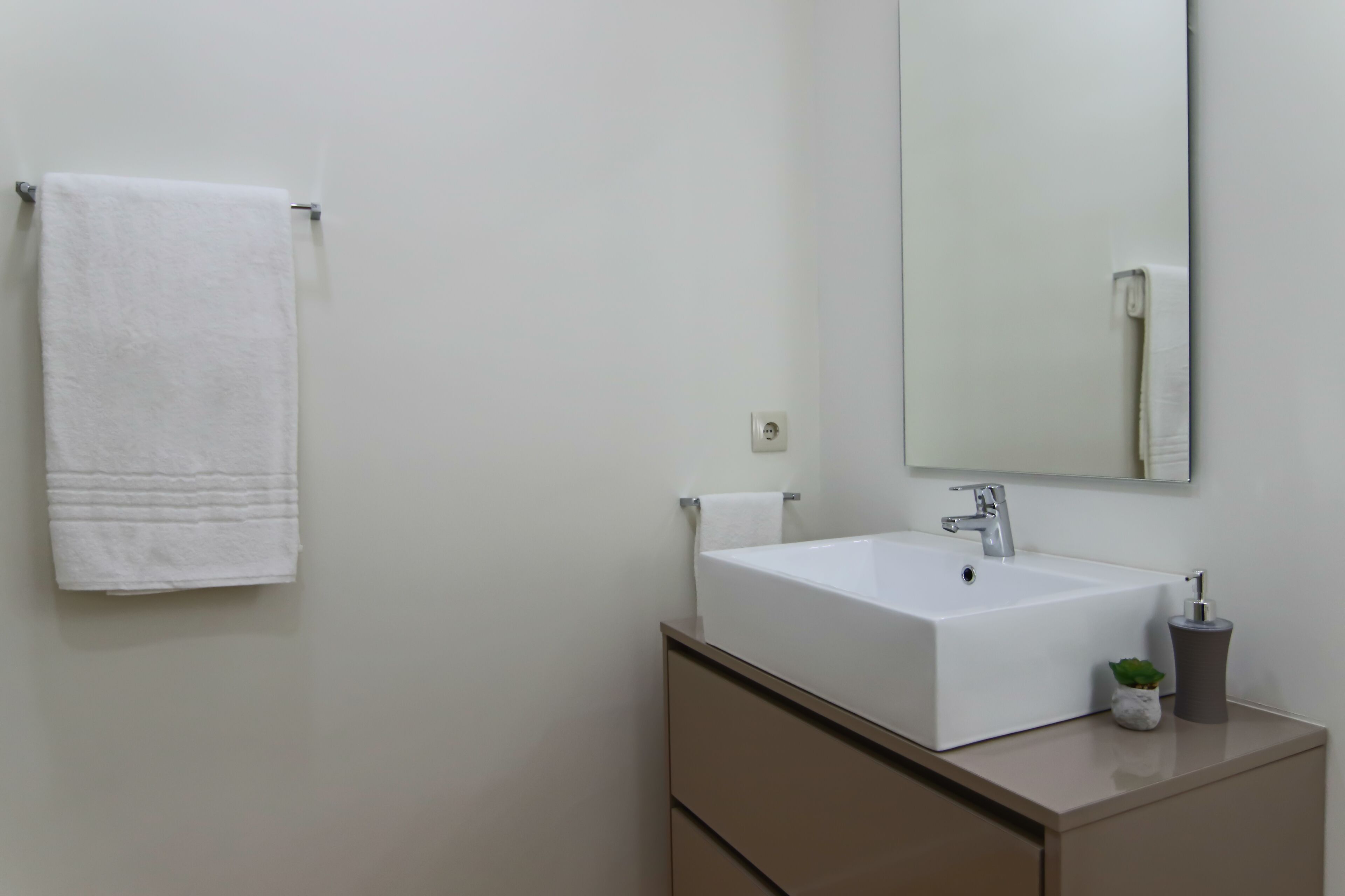 A bathroom with a white sink, a mirror, and a towel hanging on the wall.