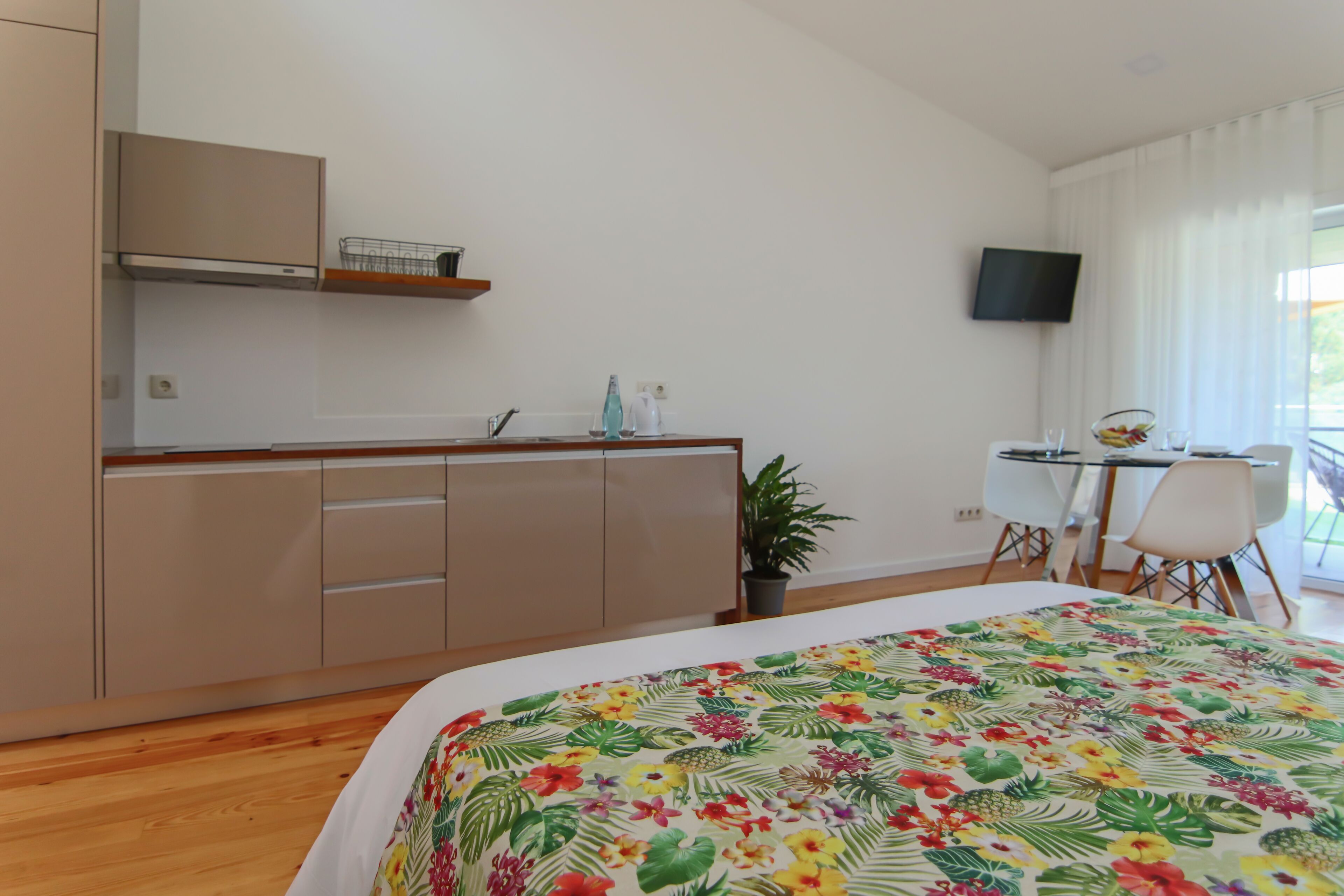 Habitación de hotel con cama, escritorio, silla, televisión y pequeña cocina.