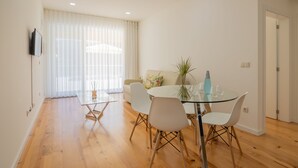A modern dining area with a glass table, white chairs, and a sofa with a floral pillow.