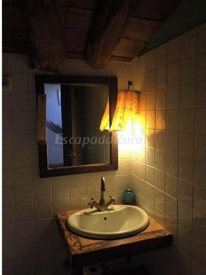 A bathroom with a wooden vanity, a mirror, and a wall-mounted light fixture. - La Valleja getaway for groups seeking serenity and natural beauty of Picos (Ruenes)