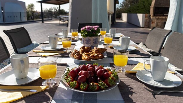Ein Frühstücksarrangement mit Croissants, Erdbeeren und Orangensaft auf einer Terrasse mit Außenbestuhlung.