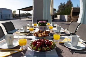 Disposição para o pequeno-almoço com croissants, morangos e sumo de laranja num terraço com área de estar ao ar livre.
