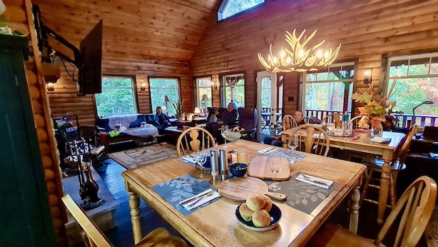 A cozy cabin interior with a dining area, wooden walls, and large windows.