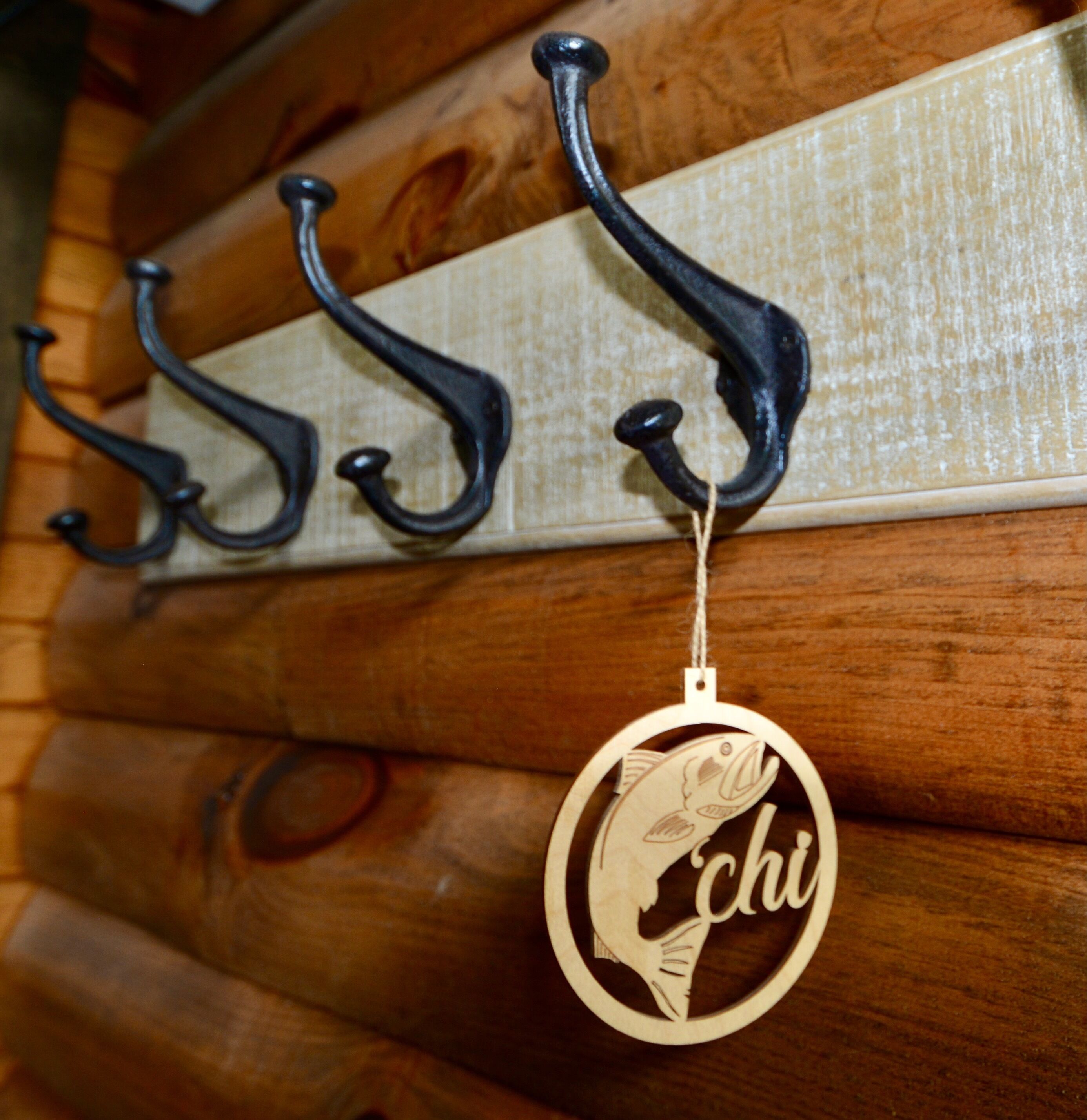 A wooden wall with three black metal hooks and a wooden fish-shaped keychain with the word "chi" on it.
