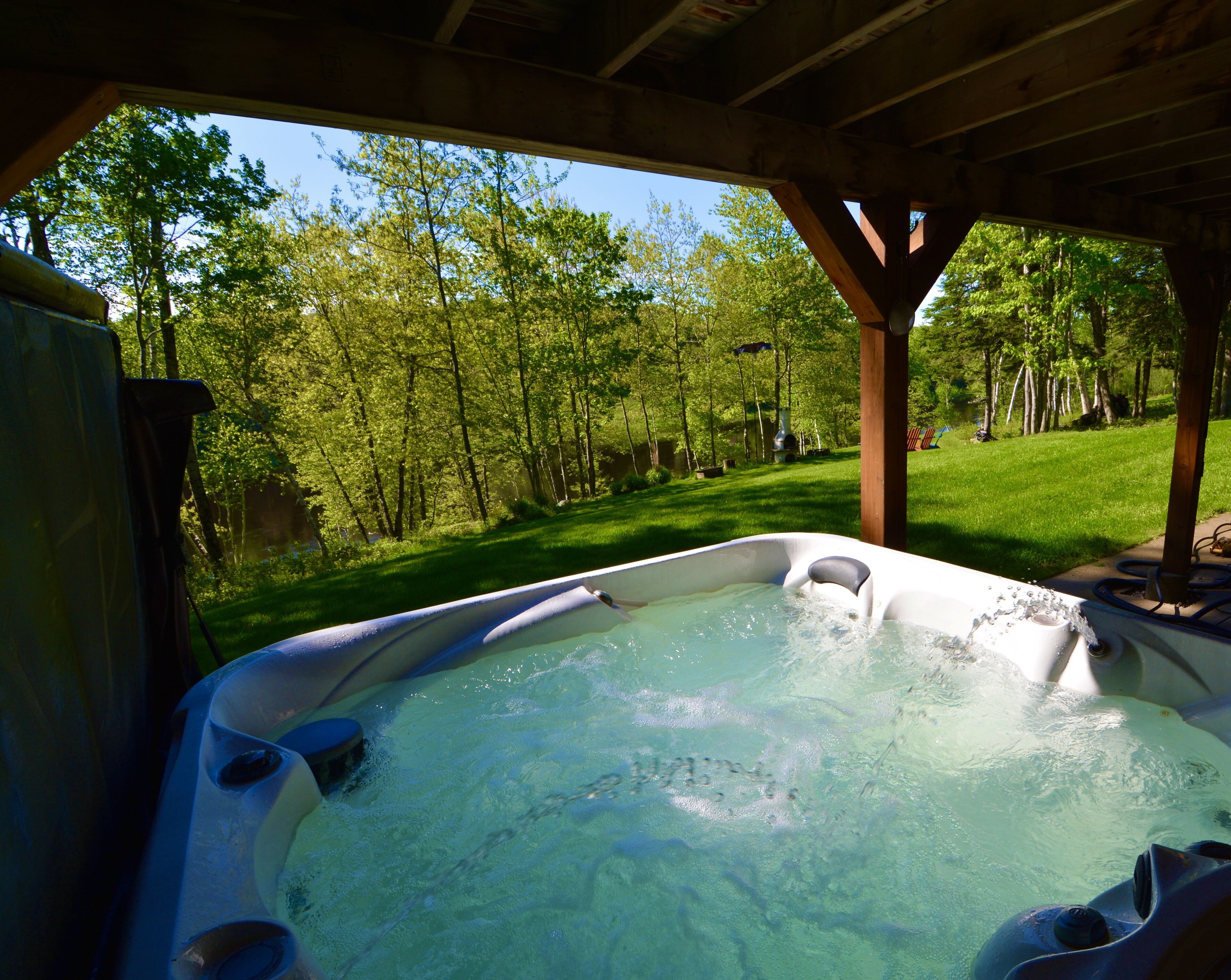 A hot tub under a wooden structure with a view of a green, wooded area.