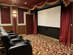 Un salón de teatro con alfombra roja, una pantalla y asientos de cuero.