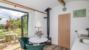 A cozy room with a round table, two chairs, a lamp, a view of the outdoors, a wooden door, and a small kitchen area. - High Rigg Shepherd's Sunrise (Brampton)