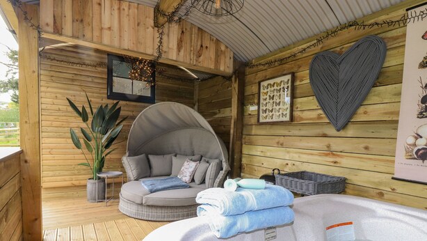 A wooden cabin with a hot tub, a cushioned seating area, and a wall-mounted heart decoration. - High Rigg Shepherd's Sunrise (Brampton)