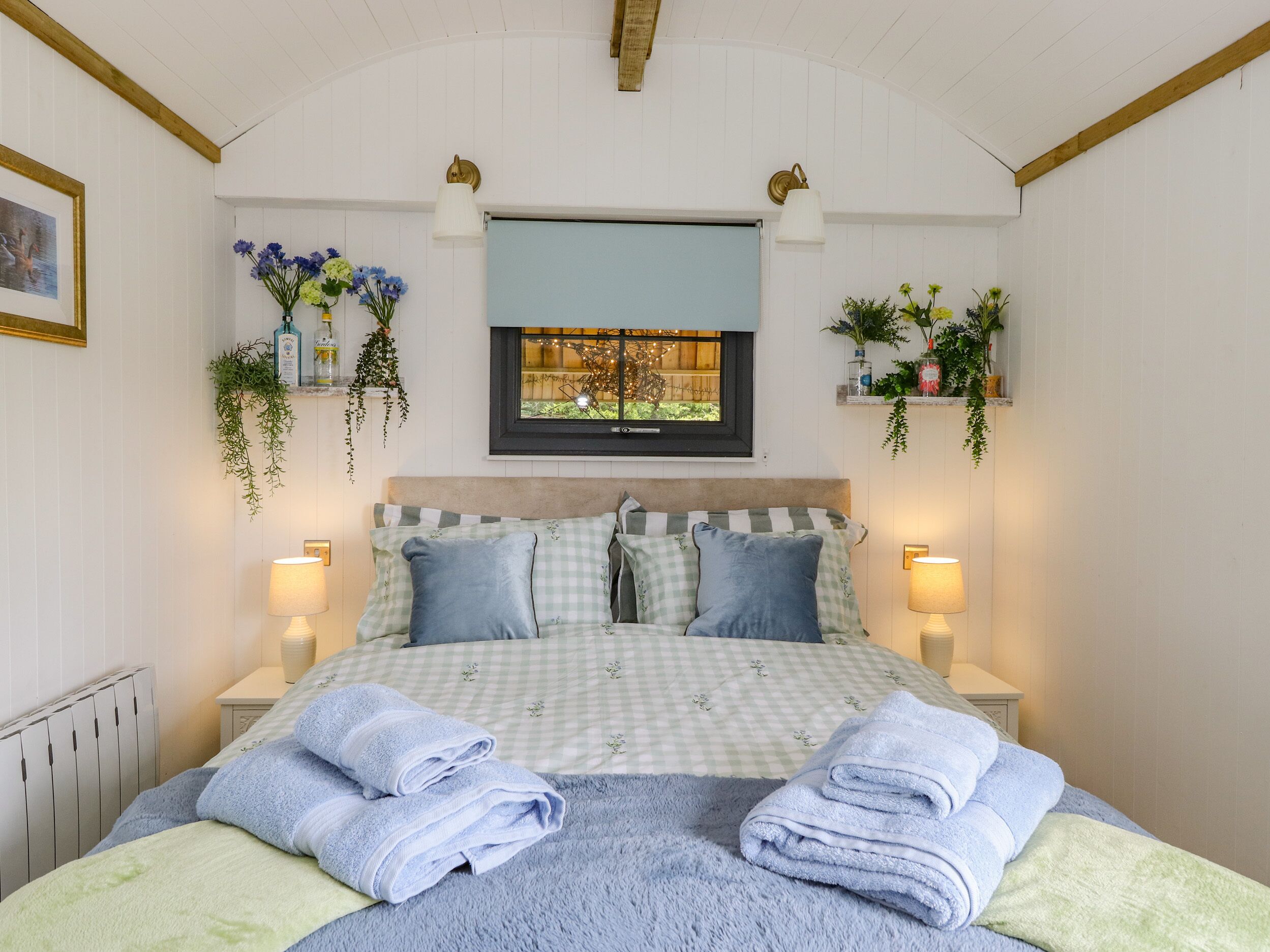 Een slaapkamer met een geruite sprei, twee bedlampen, een raam met uitzicht op groen en een radiator.