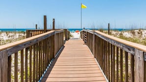 A wooden boardwalk leading to a beach with a yellow flag.