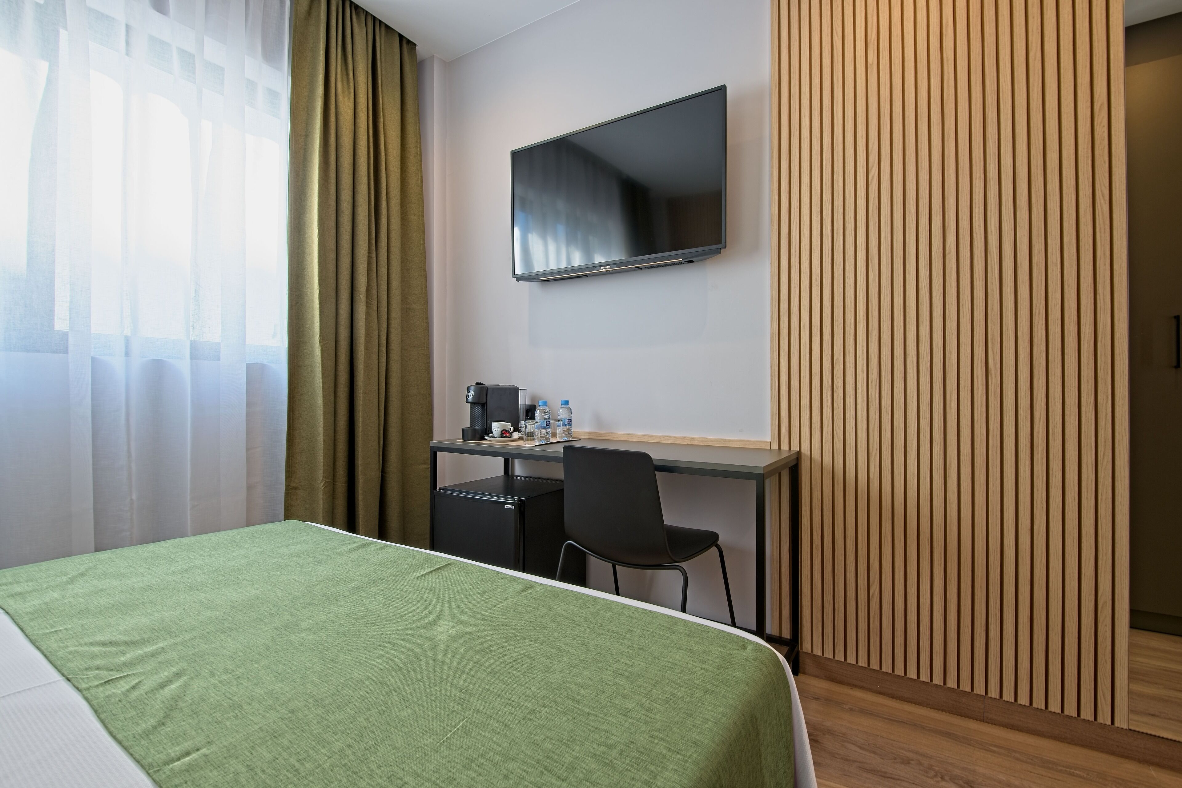 Una habitación de hotel con una cama, un escritorio con una silla, un televisor y un refrigerador pequeño.