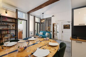 A dining area with a wooden table set for a meal, a blue sofa, and a kitchen area with a black countertop. - Troglodyte Jacuzzi in the City Centre, nearby the beach, Patio, A/C, WiFi (Collioure)