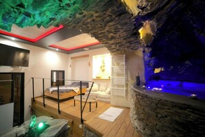 Un cuarto de spa con pared de piedra, una cama, una pequeña piscina y una terraza de madera.