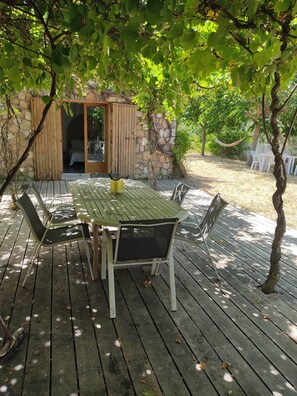 A wooden deck with a table and chairs, a stone wall, and a door leading to a room.