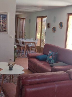 A living room with a red sofa, a white table, and a dining area with a glass door leading to a balcony.