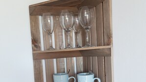 Une étagère en bois avec des verres à vin, deux tasses en forme de cœur et une bougie.