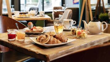 Una mesa de desayuno con cruasanes, fruta y té, en un café con mesa y sillas de madera.