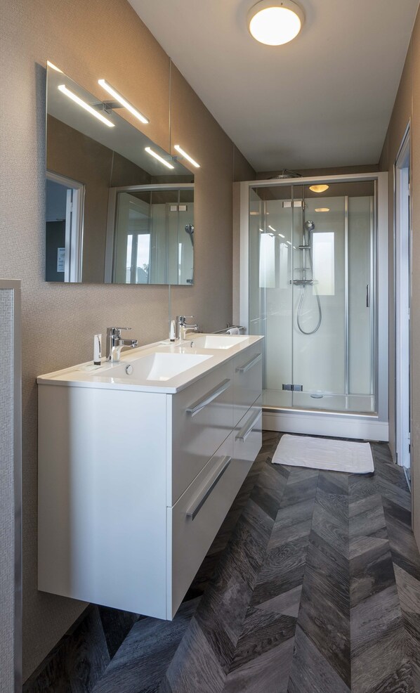 Un baño moderno con tocador doble, cabina de ducha de vidrio y suelo con patrón de espiga.