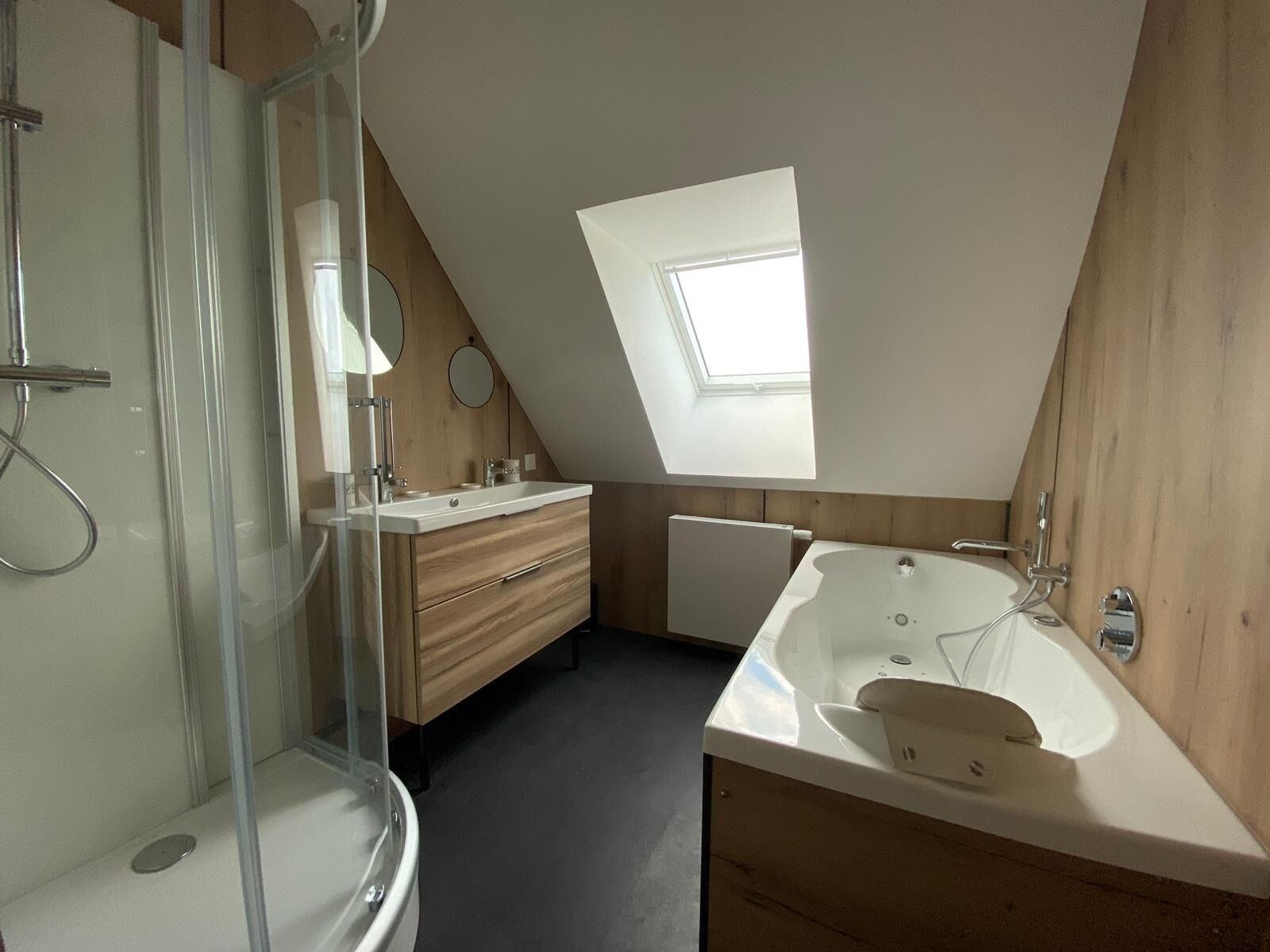 Un baño moderno con tragaluz, ducha a ras de suelo, bañera independiente y muebles de madera.