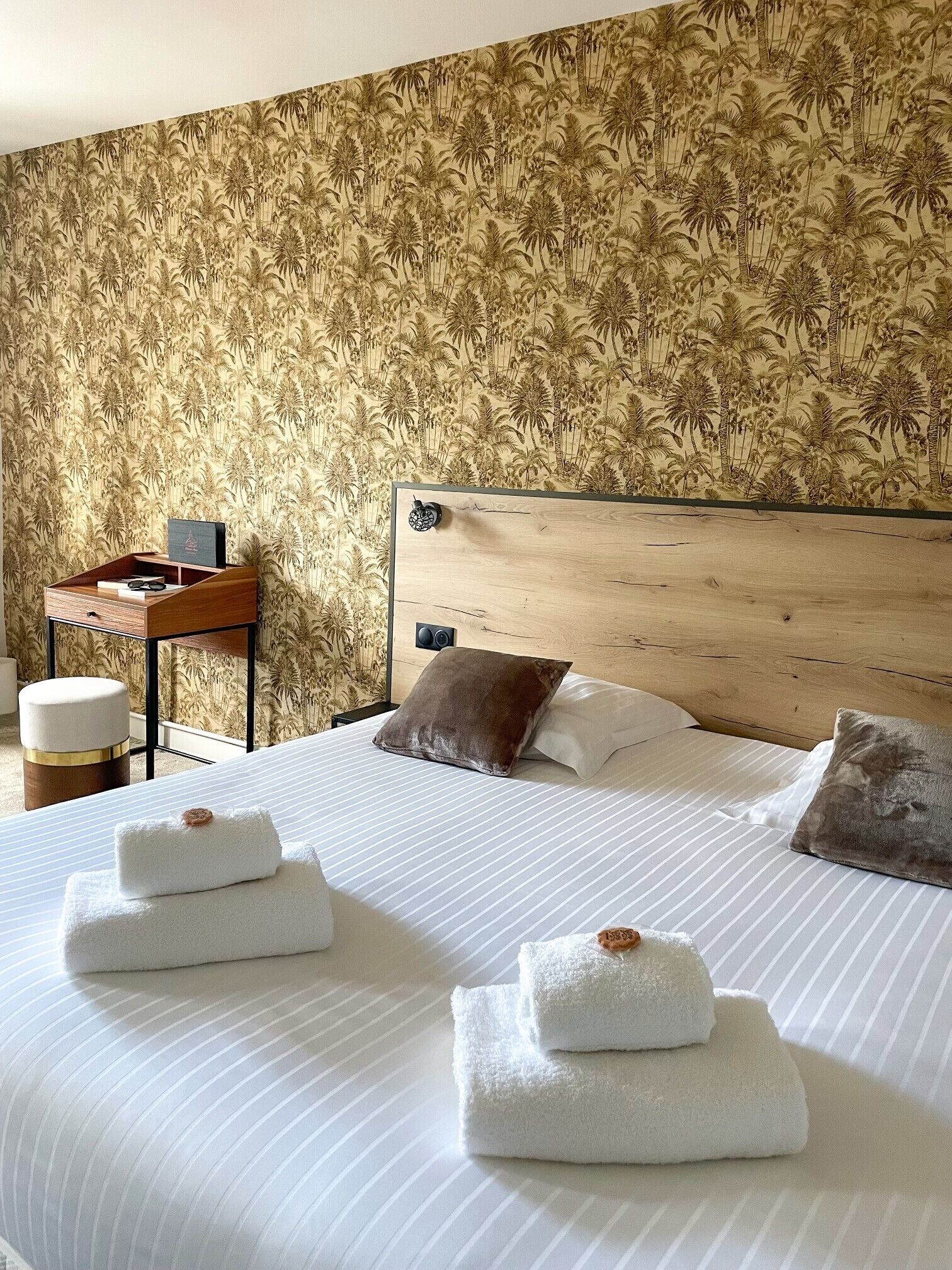 Habitación de hotel con cama, almohadas, mesita de noche con lámpara y pared con estampado de motivos tropicales.