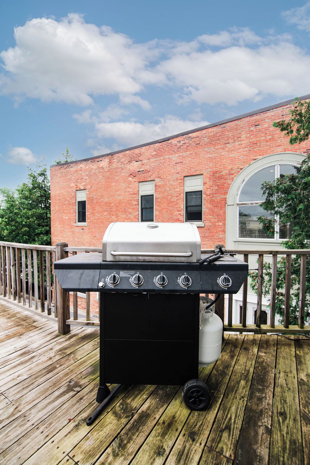 Een barbecue op een houten terras met een bakstenen gebouw op de achtergrond.