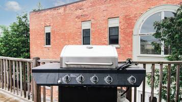 Een barbecue op een houten terras met een bakstenen gebouw op de achtergrond.