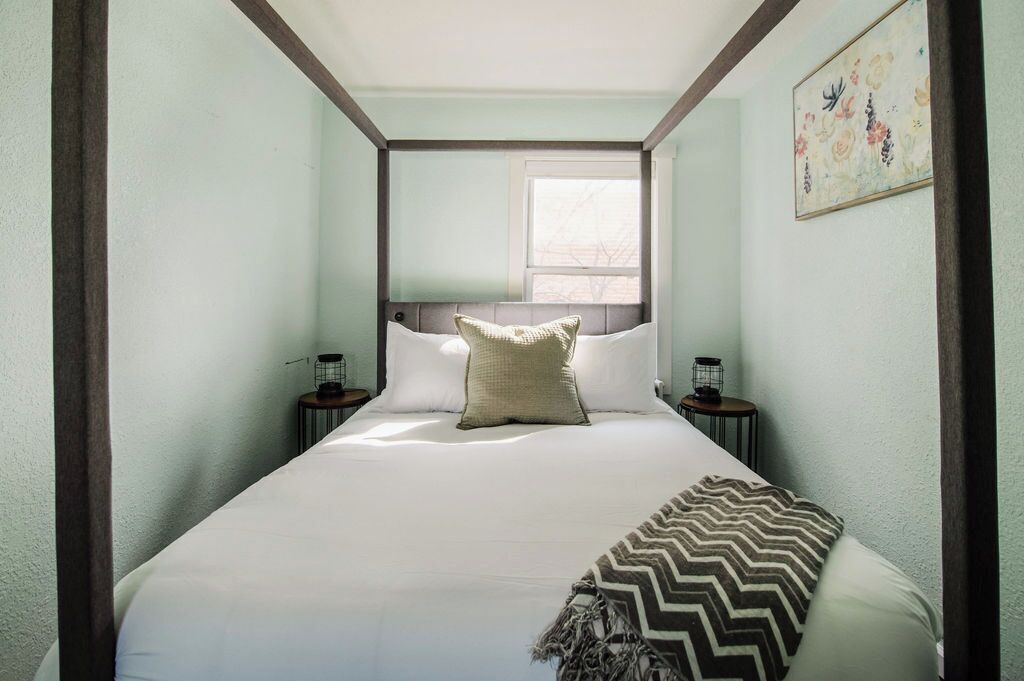 A narrow room with a bed, two bedside tables, a window, and a wall-mounted artwork.