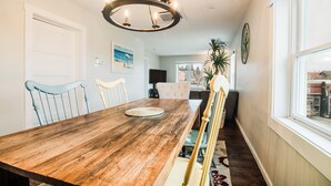 Comedor con mesa de madera, sillas, una lámpara de araña y vista al exterior a través de una ventana.