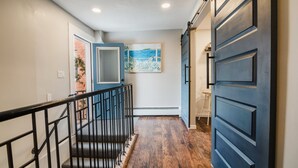 Un pasillo con piso de madera, una puerta azul y una escalera con barandillas negras.