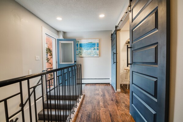 A hallway with a wooden floor, a blue door, and a staircase with black railings.