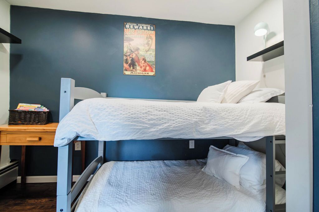 Une chambre avec un lit superposé, une affiche accrochée au mur, un bureau avec un panier et une table de chevet avec une lampe.