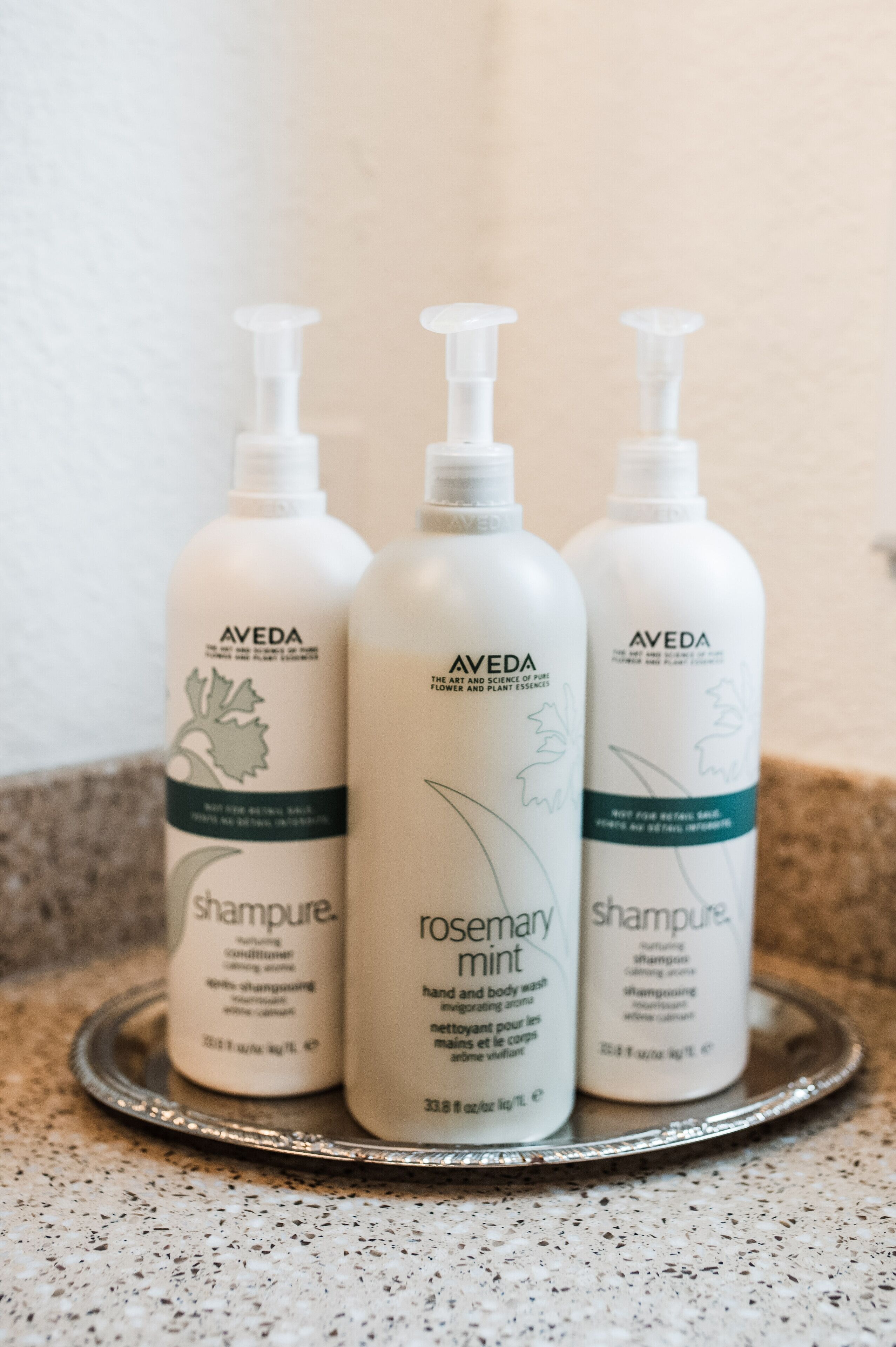 Tres botellas de champú y gel de baño Aveda sobre una bandeja.