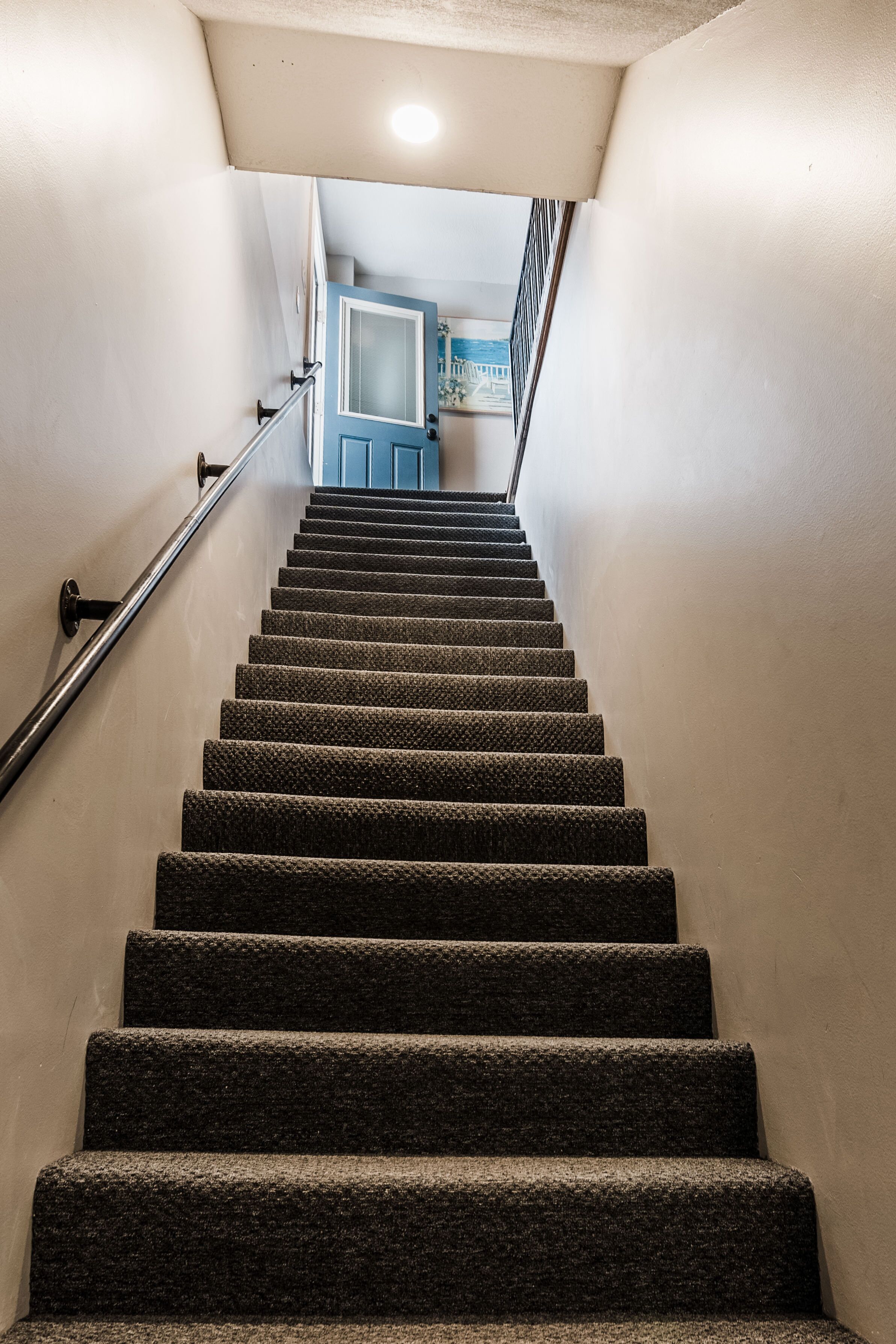 Eine Teppichstiege mit Handlauf, die zu einem Raum mit blauer Tür und einem gerahmten Bild an der Wand führt.