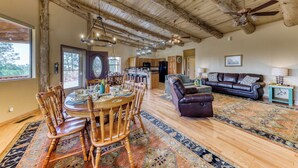 A spacious living area with a wooden ceiling, a dining table with chairs, a leather sofa, and a patterned rug. - White Mountain Retreat by Ruidoso Vacation Rentals (Ruidoso)