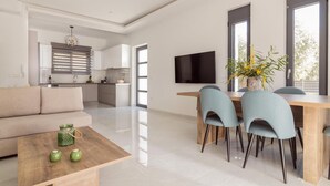 A modern living space with a sofa, dining table, chairs, a TV, and a kitchen area.