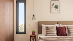 A bedroom with a bed, a window, a wall-mounted light, and a small table with a plant.
