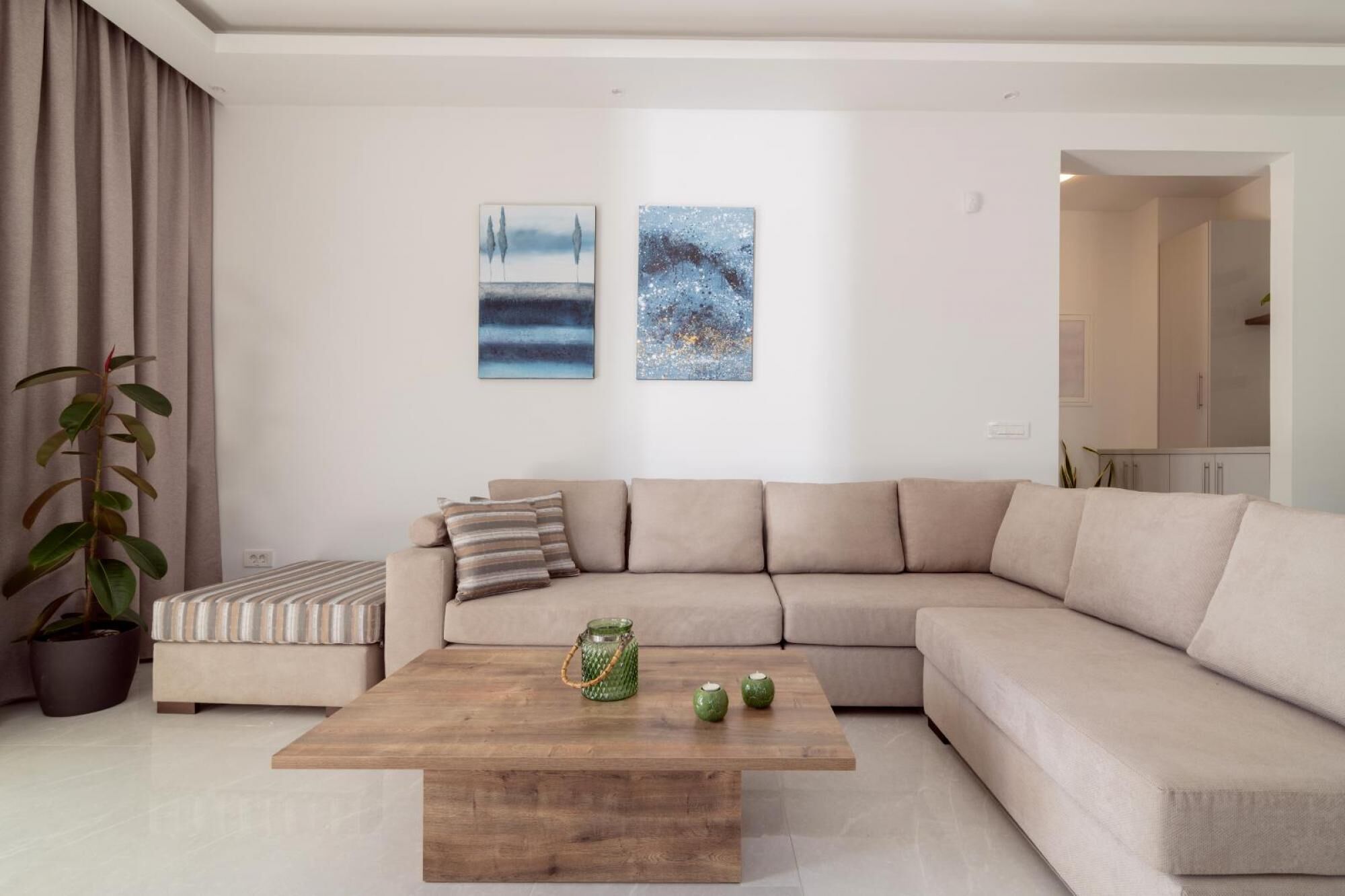 Een moderne woonkamer met een beige hoekbank, een houten salontafel en twee abstracte schilderijen aan de muur.