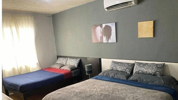 Un dormitorio con dos camas individuales, una mesita de noche con lámpara y aire acondicionado instalado en la pared.