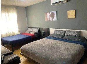 Een slaapkamer met twee eenpersoonsbedden, een nachtkastje met een lamp, en een luchtverkoeler aan de muur.