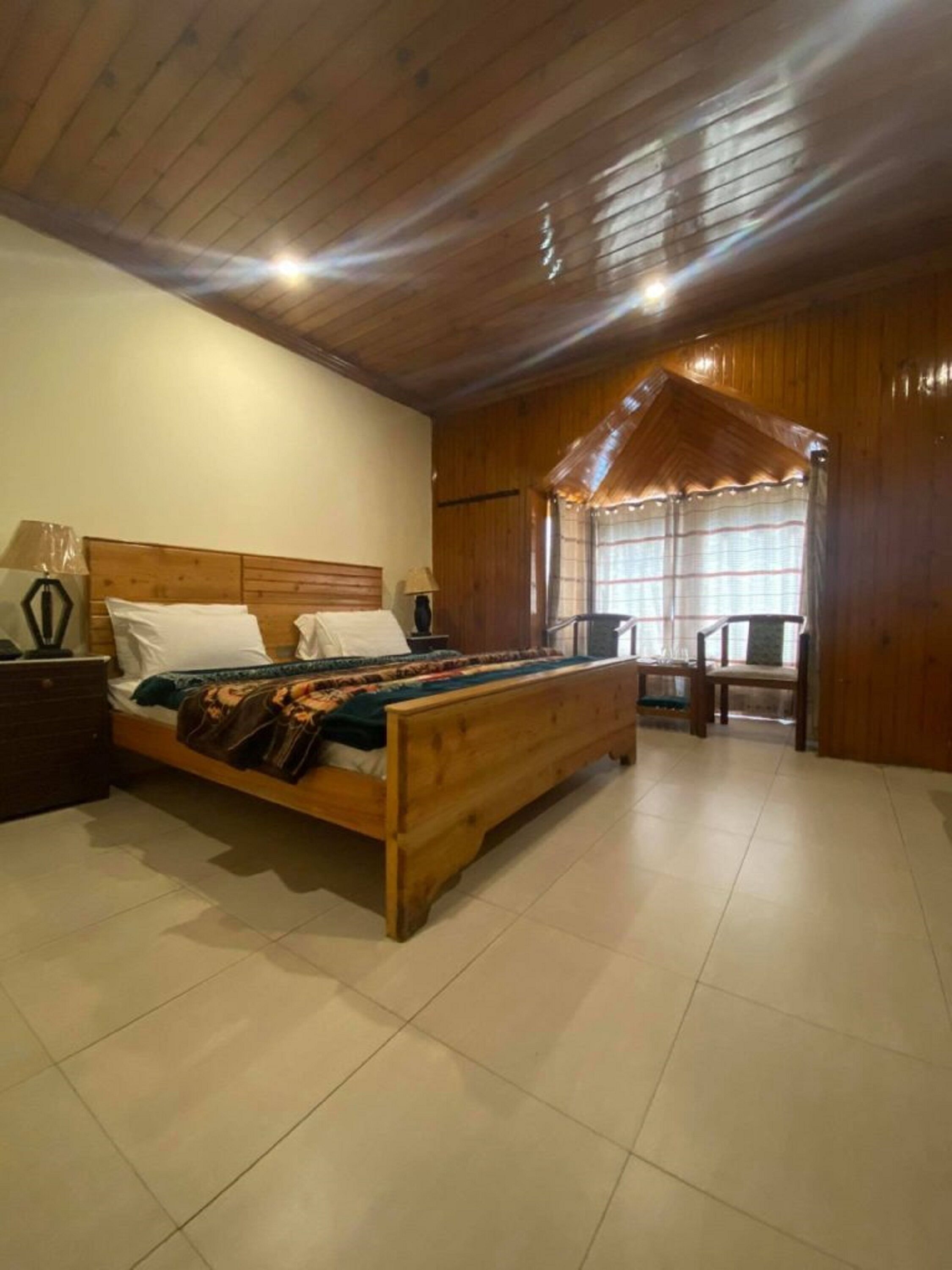 A bedroom with a wooden bed, a nightstand, a chair, and a window with curtains.