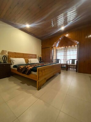 A bedroom with a wooden bed, a nightstand, a chair, and a window with curtains.