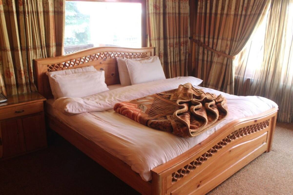 A wooden bed with a headboard, a bedside table, and a window with curtains.