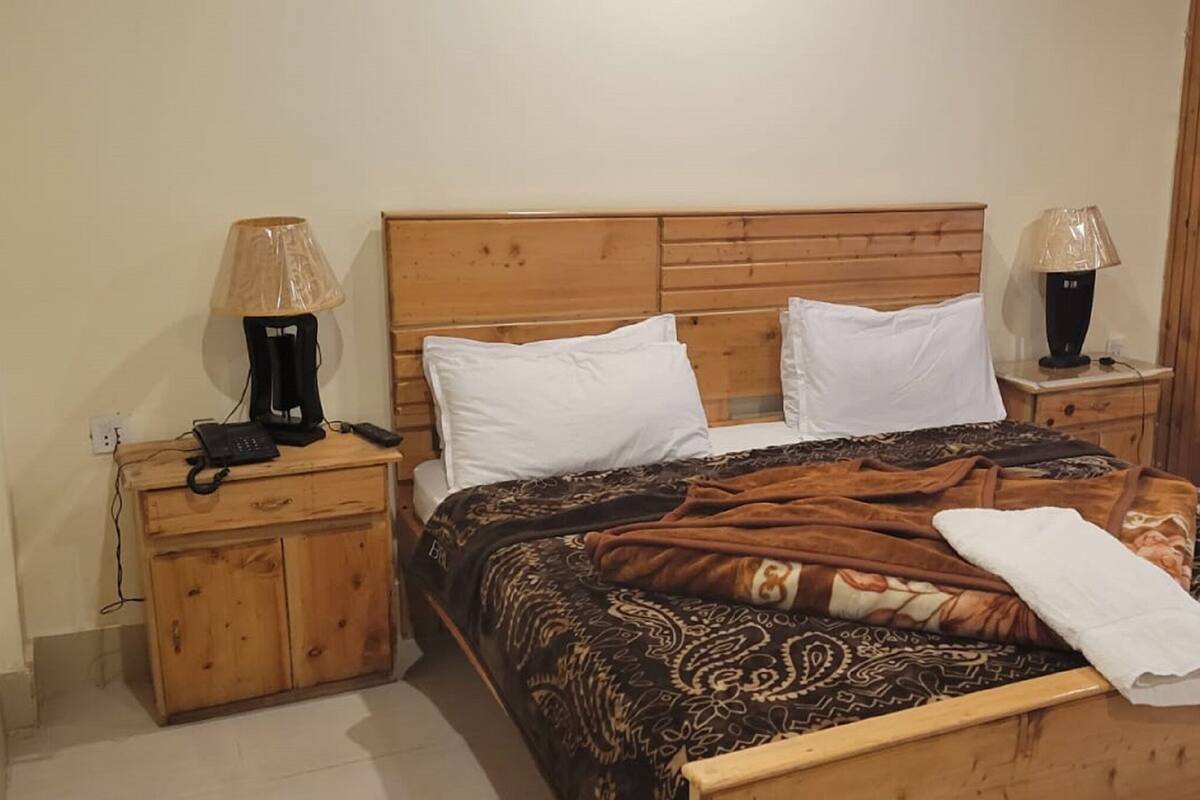 A wooden bed with a patterned blanket, two bedside lamps, and a wooden nightstand with a phone.